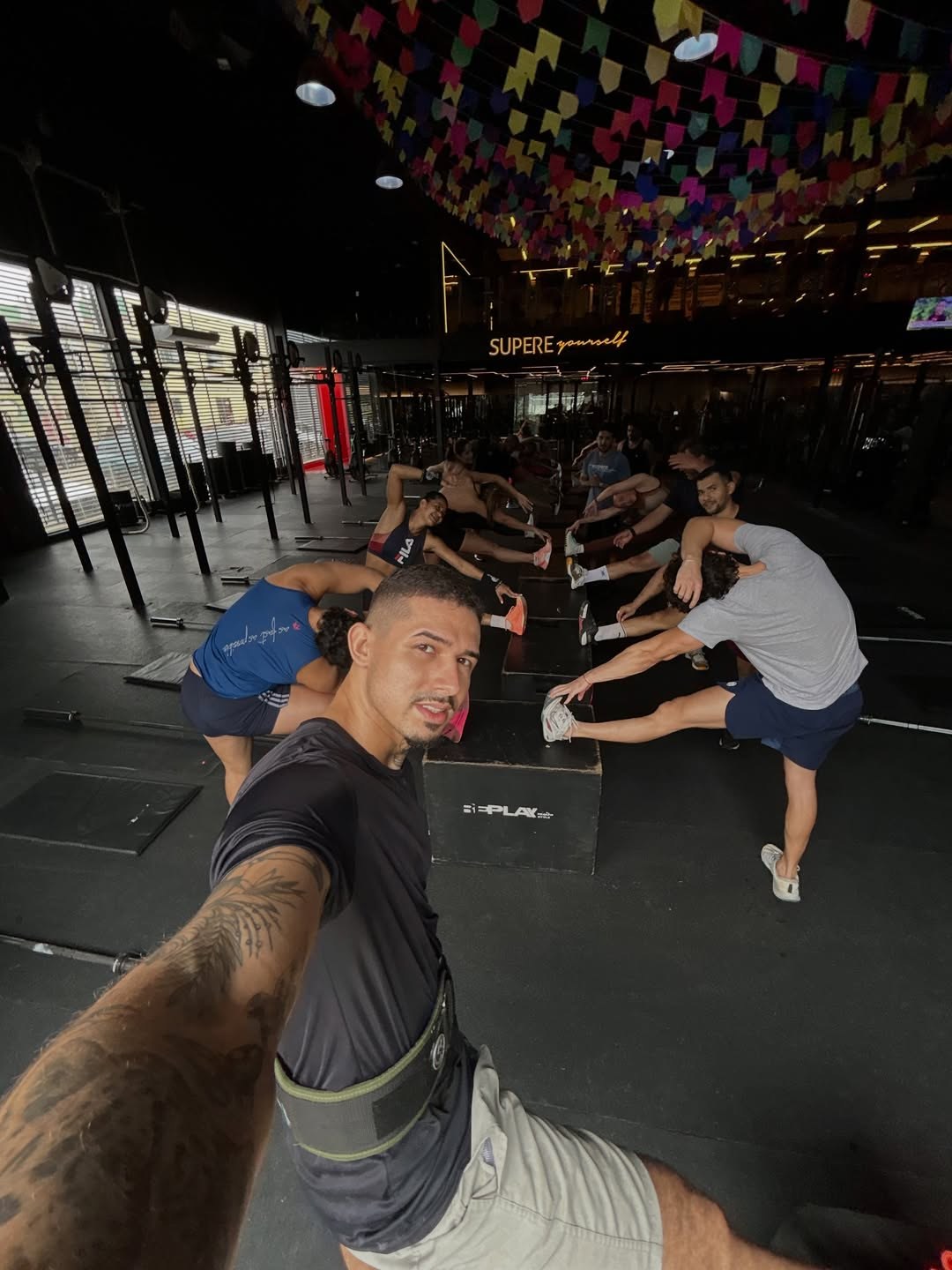 Diego em primeiro plano no box, com um grupo se alongando ao fundo
